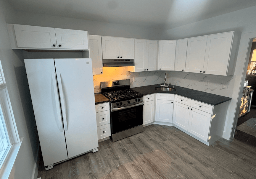 L-shaped white kitchen with dark countertops and a gas range