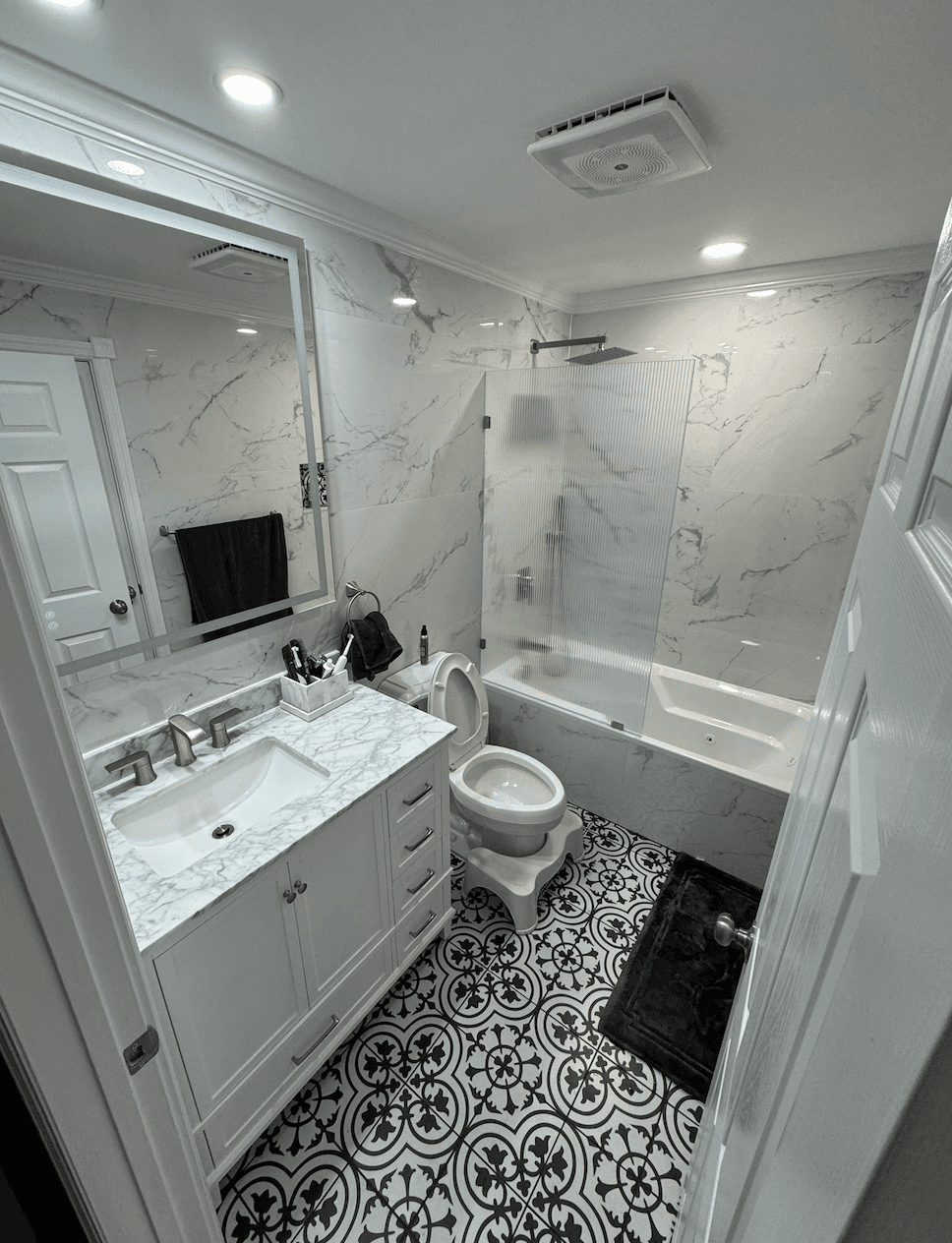 Bathroom with patterned black and white floor tile, white vanity and tub