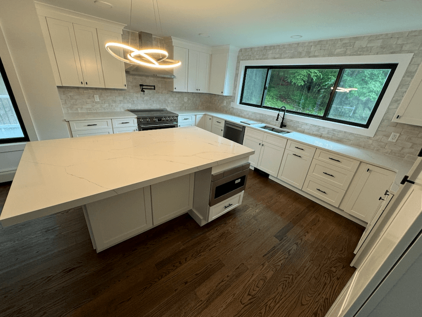 Remodeled kitchen with a white quartz island, ring pendant light and hardwood floor