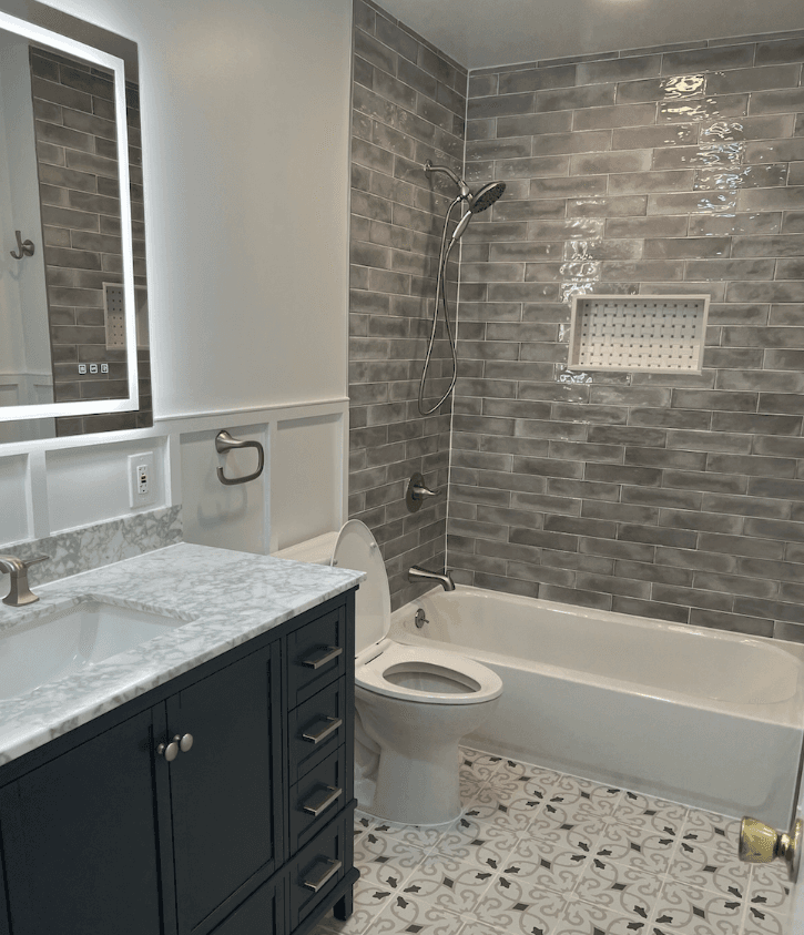 Bathroom with gray brick-pattern shower tile, navy vanity and marble top